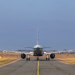 A rear view of a commercial airplane taxiing on a runway under a clear sky.