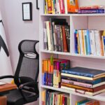 A modern office space with a bookshelf filled with colorful books and an ergonomic chair.