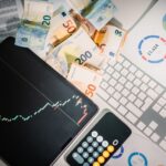 Overhead view of financial tools with Euro banknotes on a desk showing market trends and graphs.