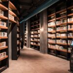 A spacious library featuring tall wooden bookshelves filled with books and ambient lighting.